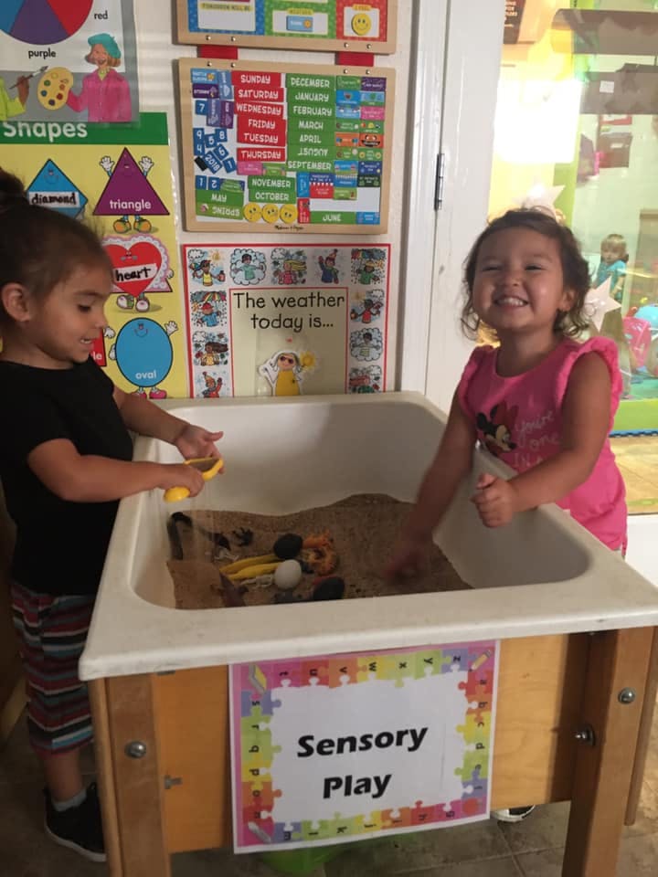 Two children playing at a sensory table with sand