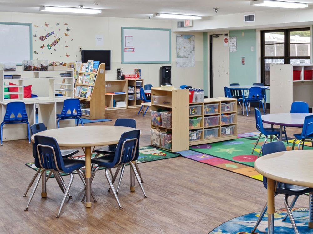 Empty classroom with small tables and chairs, shelves, and colorful rugs