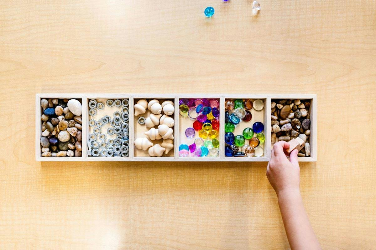 Hand placing a small wooden block into a multi-section organizer tray