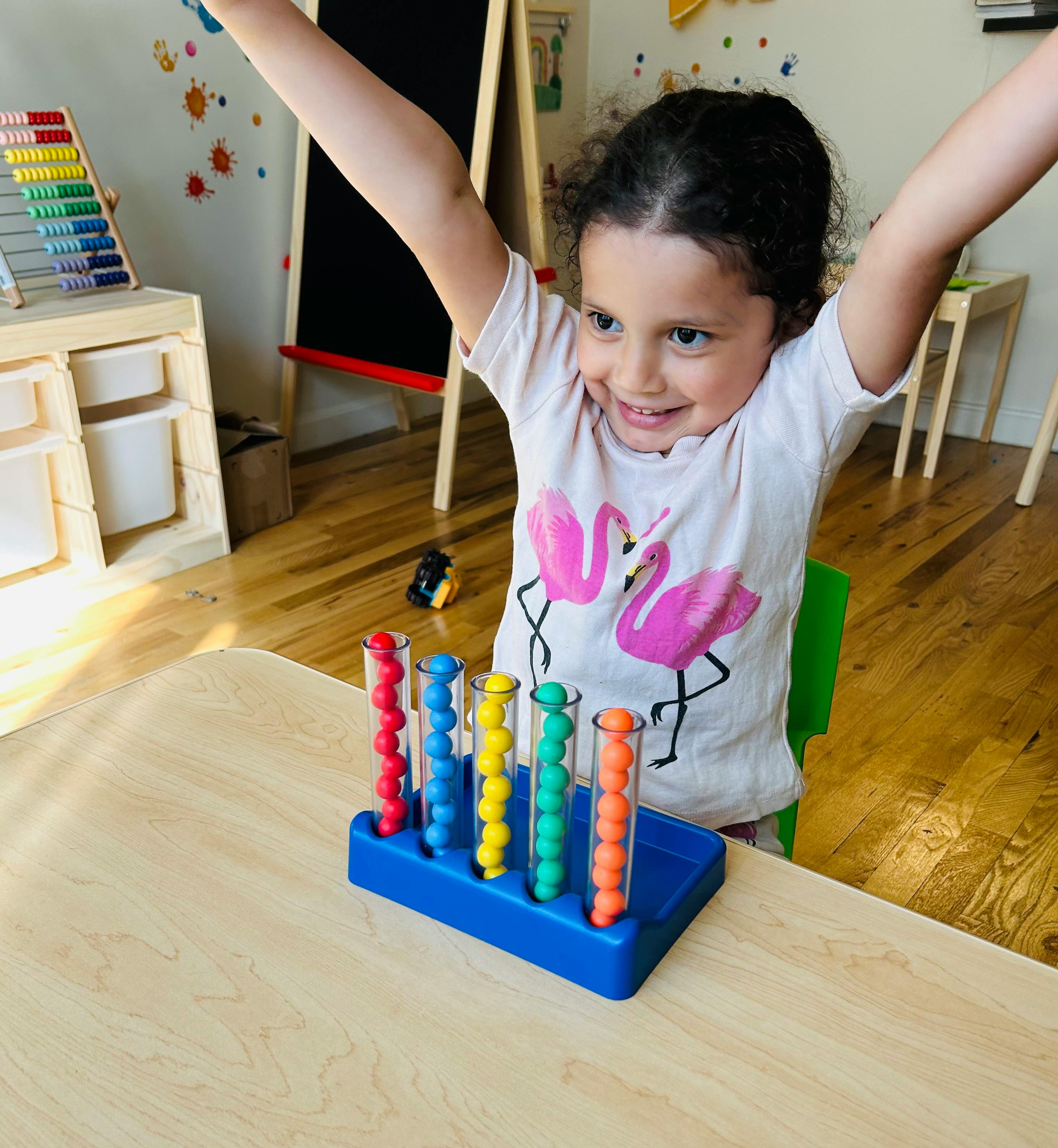 Child with arms raised, sitting at a table with a colorful bead sorting toy