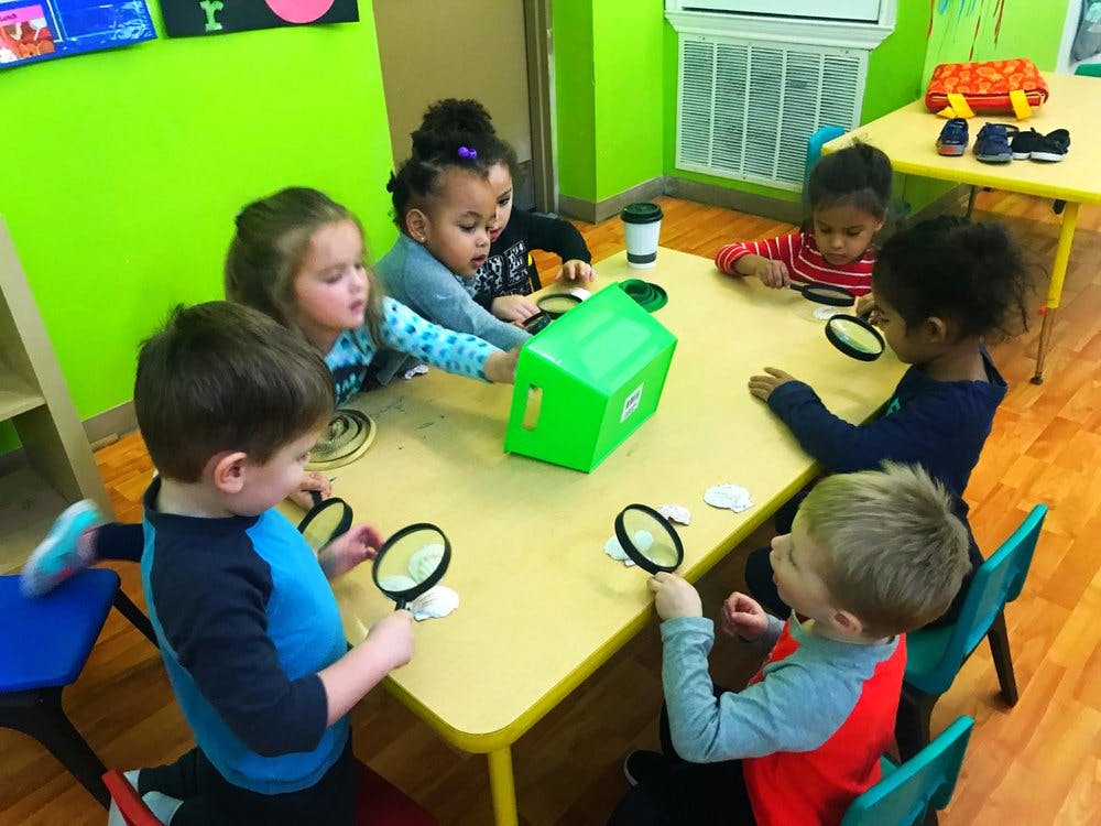 Children at a table with magnifying glasses and a green box