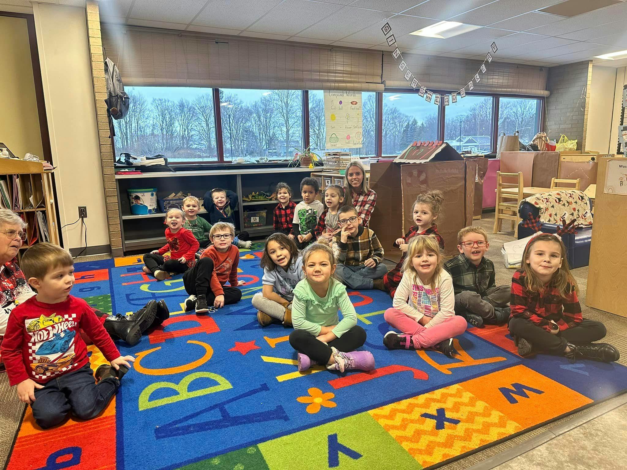 Group of children and adults sitting on a colorful alphabet rug in a classroom