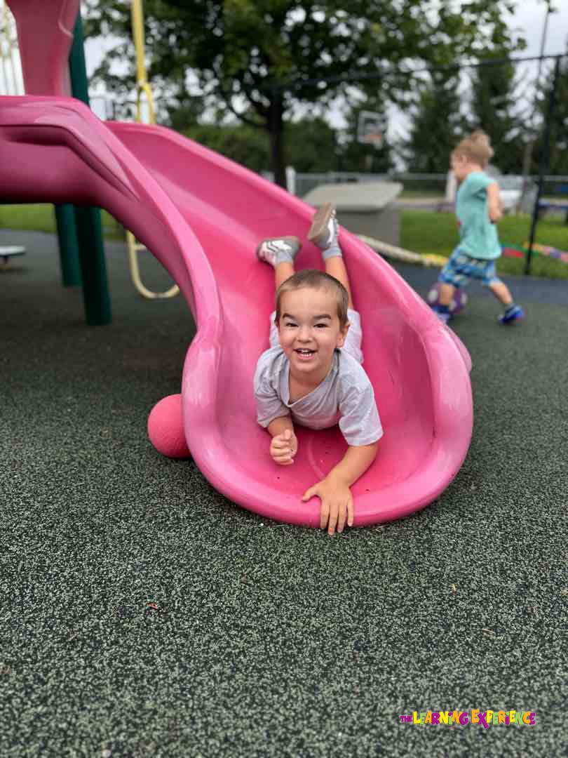 Child lying on stomach at the bottom of a pink playground slide