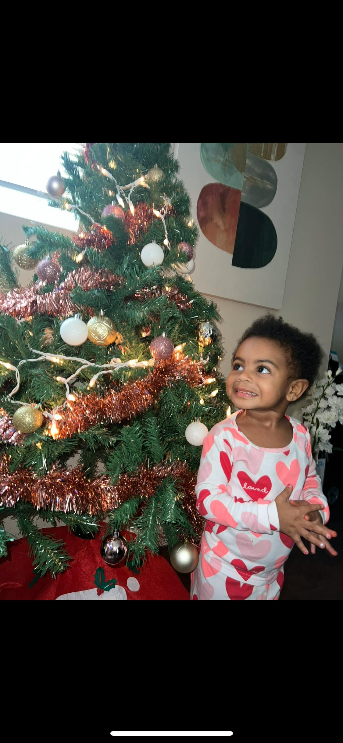 Child in heart-patterned pajamas standing next to a decorated Christmas tree