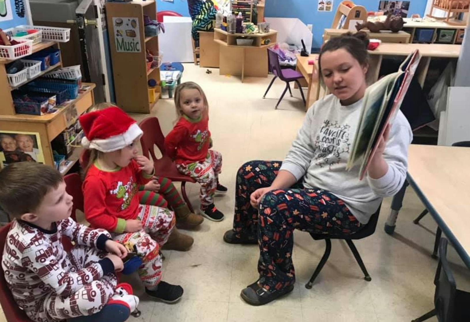 Person reading a book to three children in a classroom
