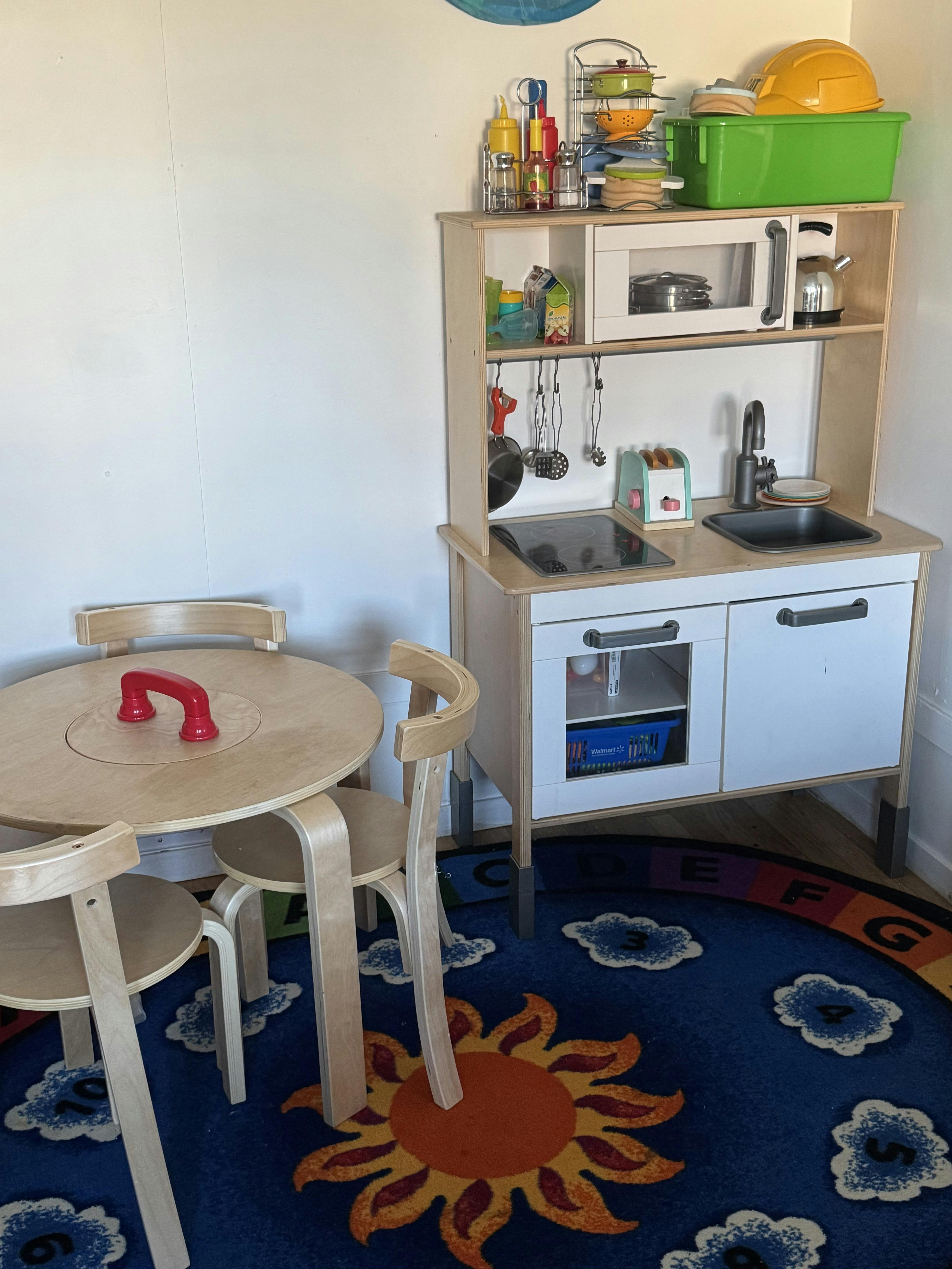 Children's play kitchen and small table with chairs on a sun and clouds rug