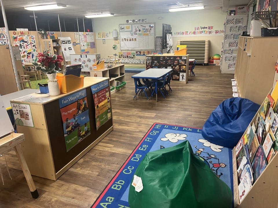 Classroom with tables, chairs, shelving units, an alphabet rug, and beanbag chairs