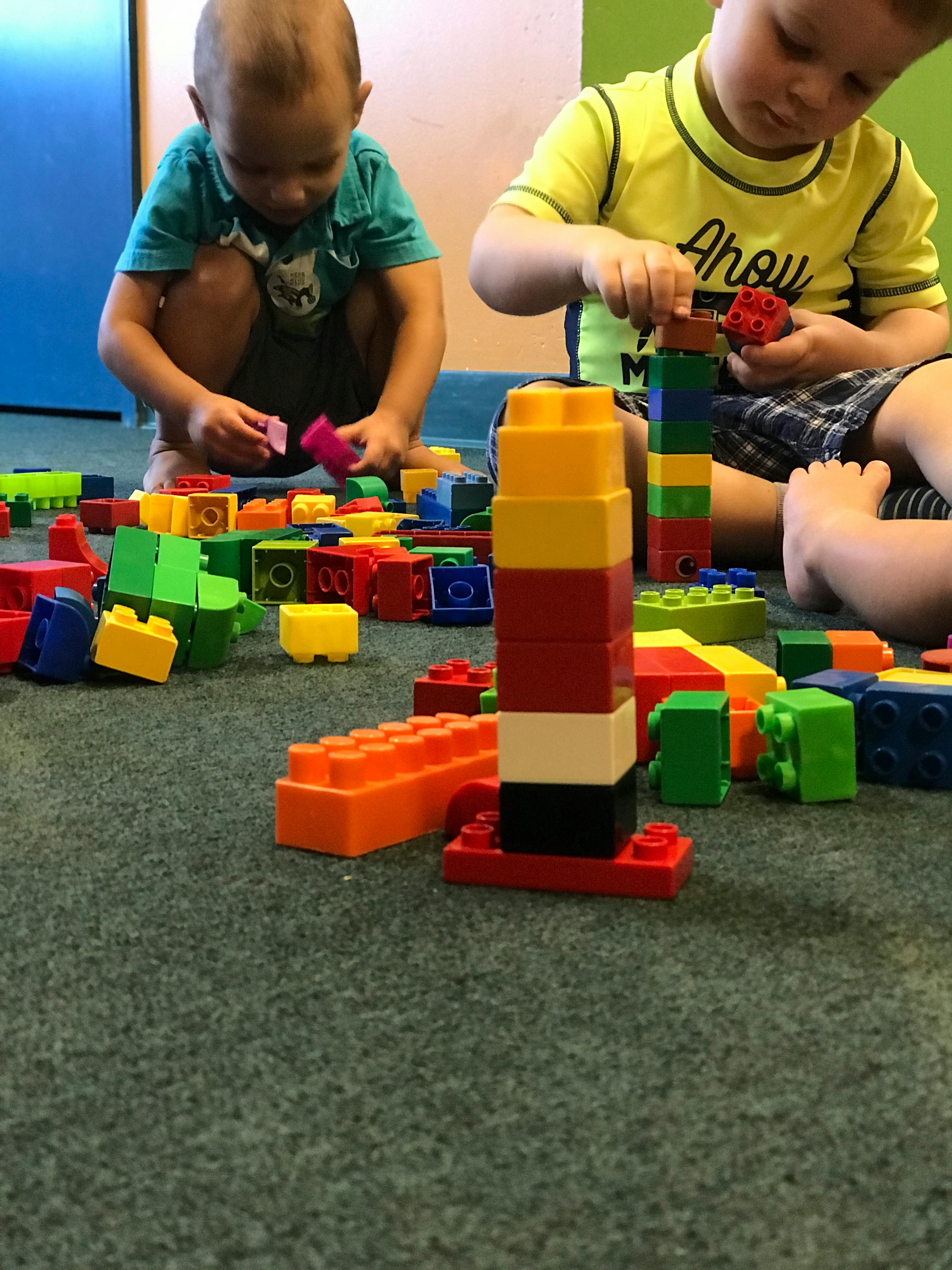 Two children playing with colorful building blocks on a carpeted floor
