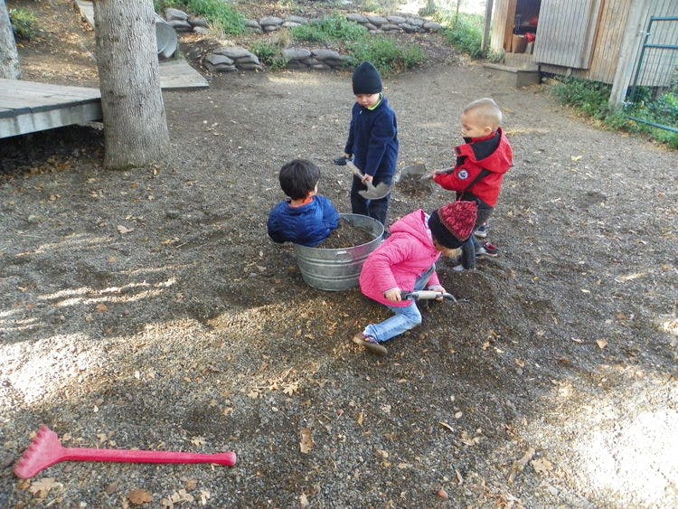Four children playing in dirt with a metal tub and plastic bucket