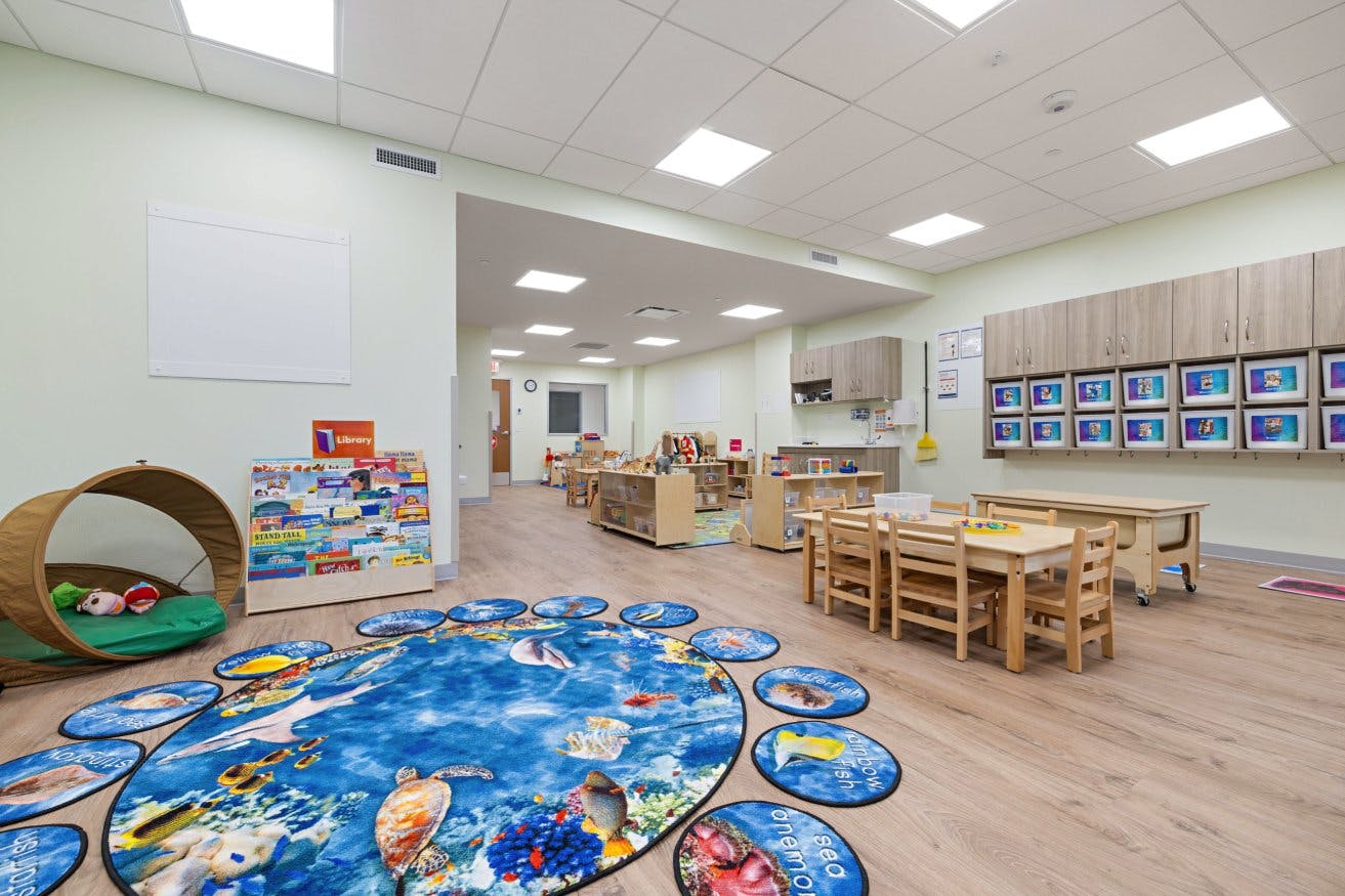 A playroom with small wooden tables and chairs, and an ocean-themed rug