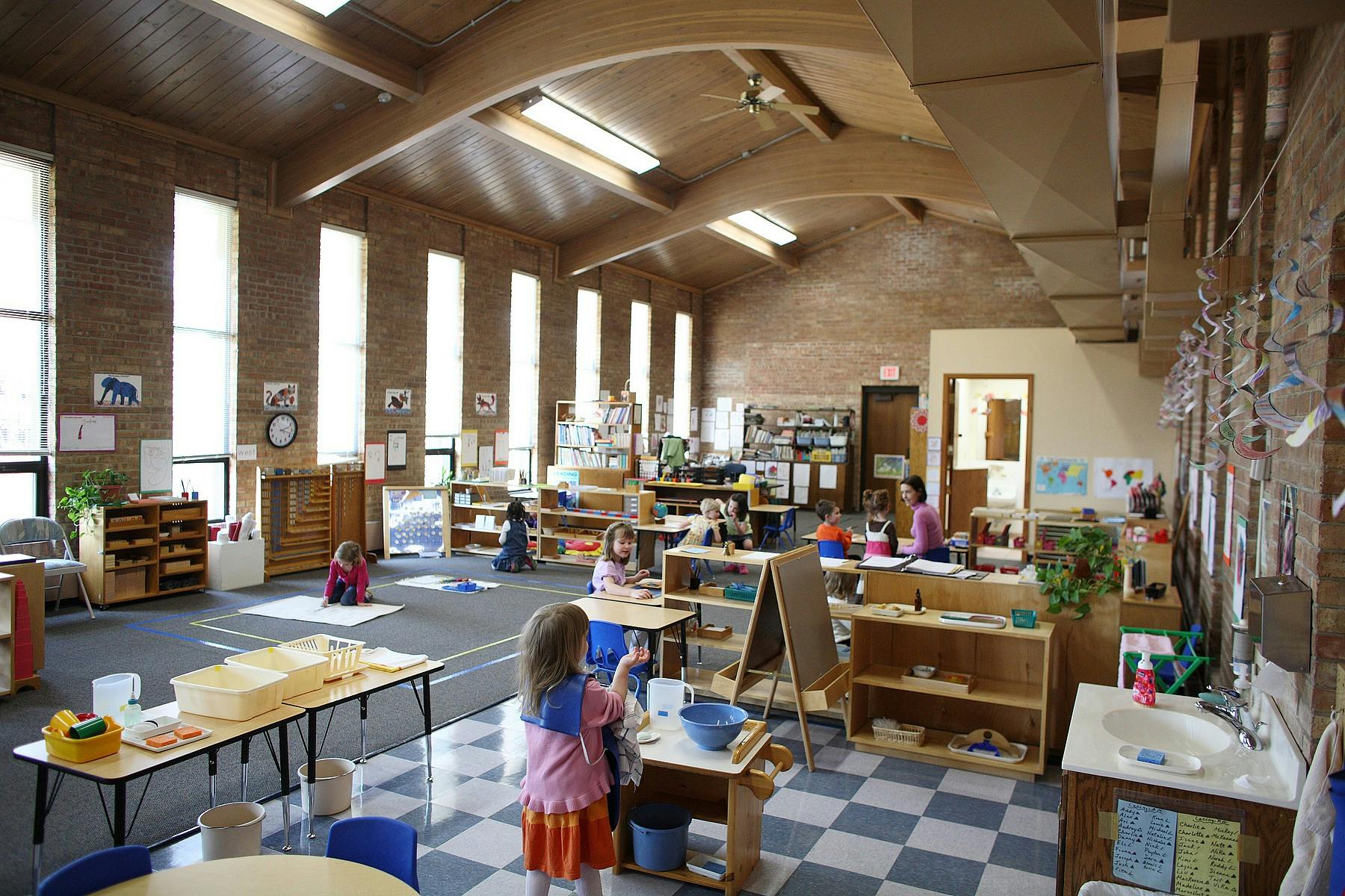 Children in a classroom with tables, shelves, and a checkered floor