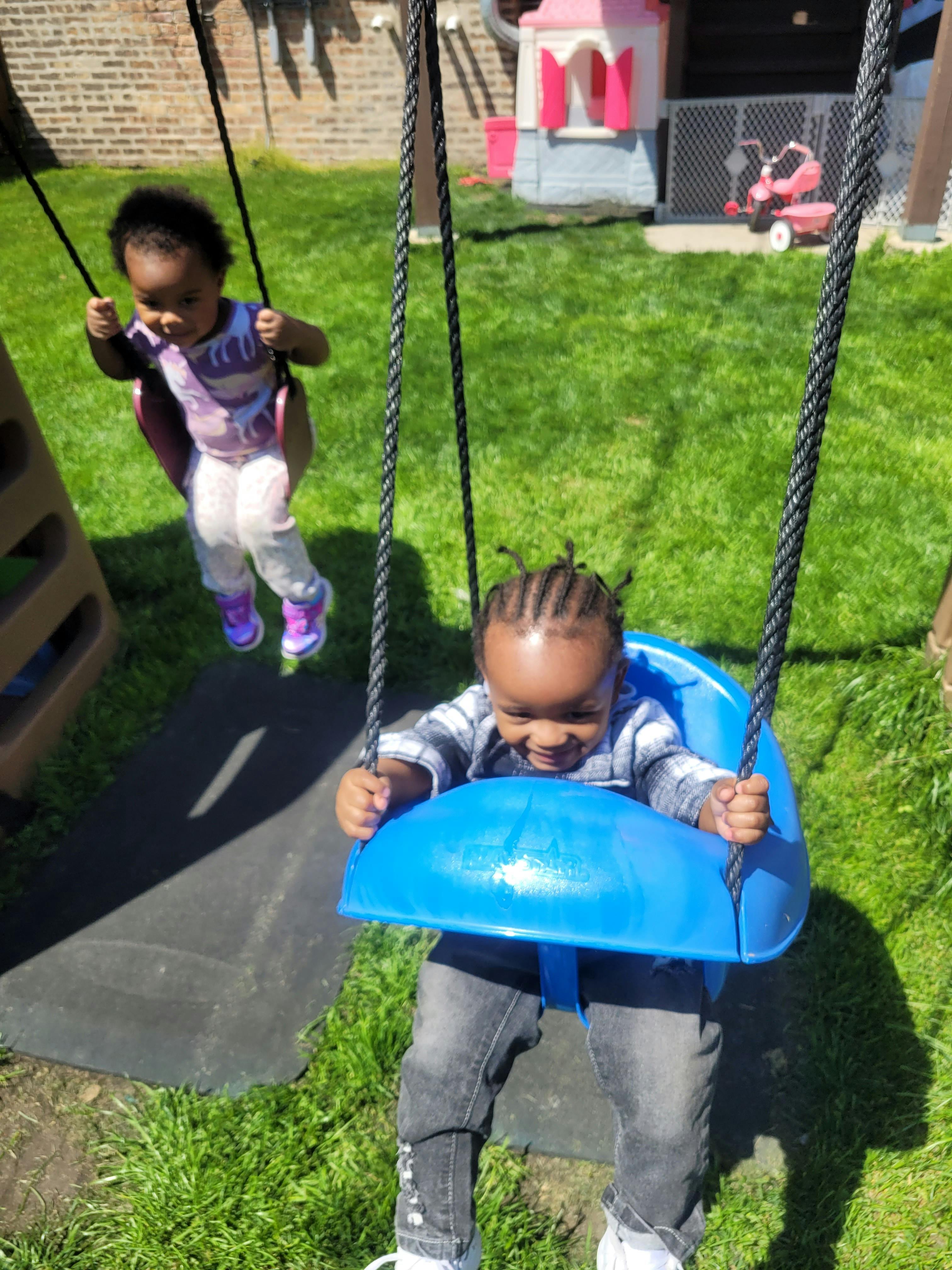 Two children on swings in a grassy yard