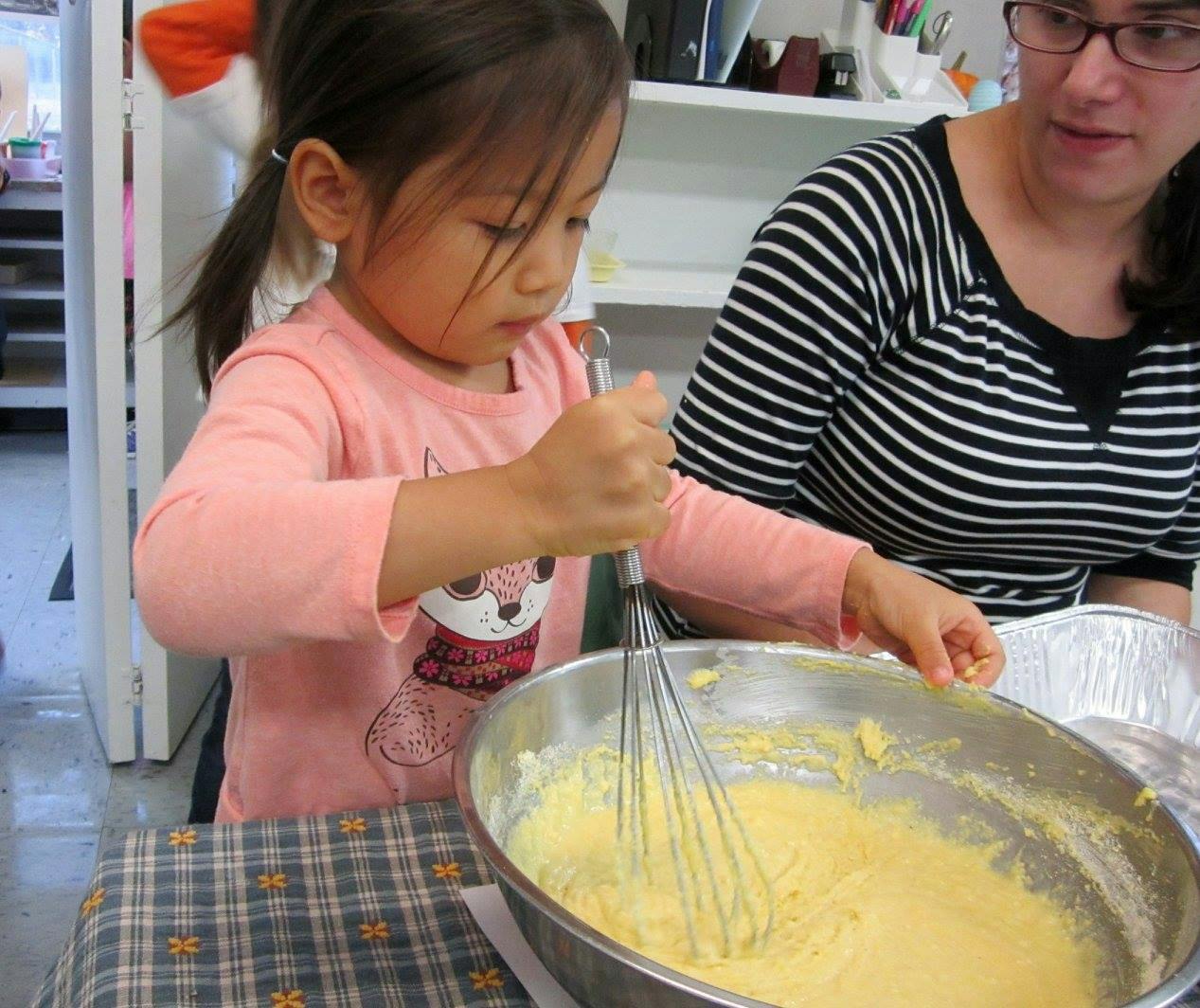 Child whisking batter in a bowl with an adult nearby