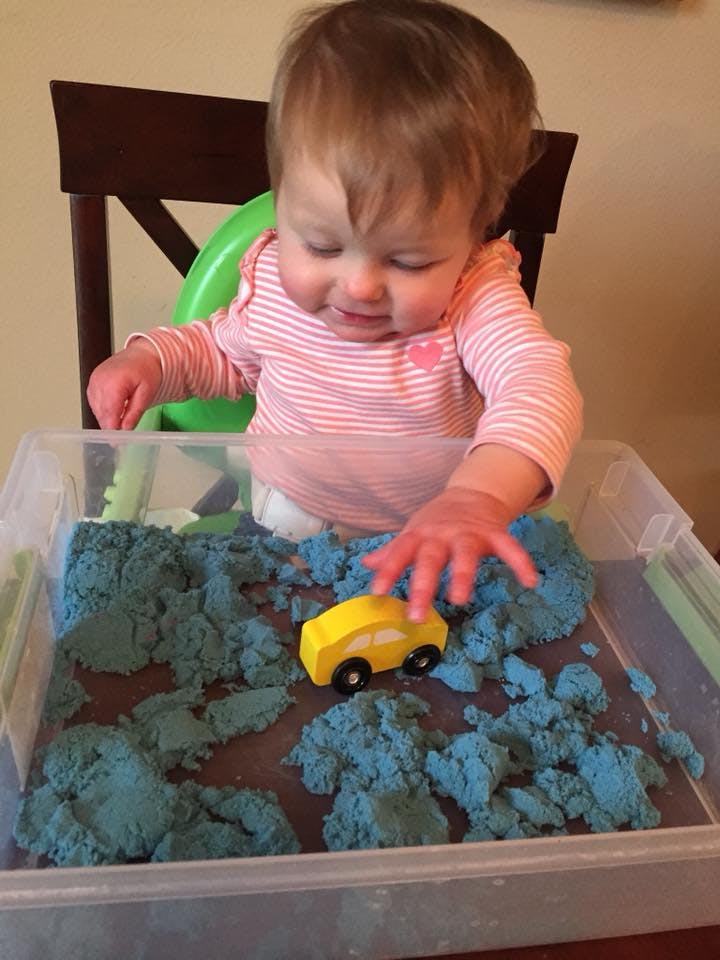 Child playing with a yellow toy car in blue kinetic sand