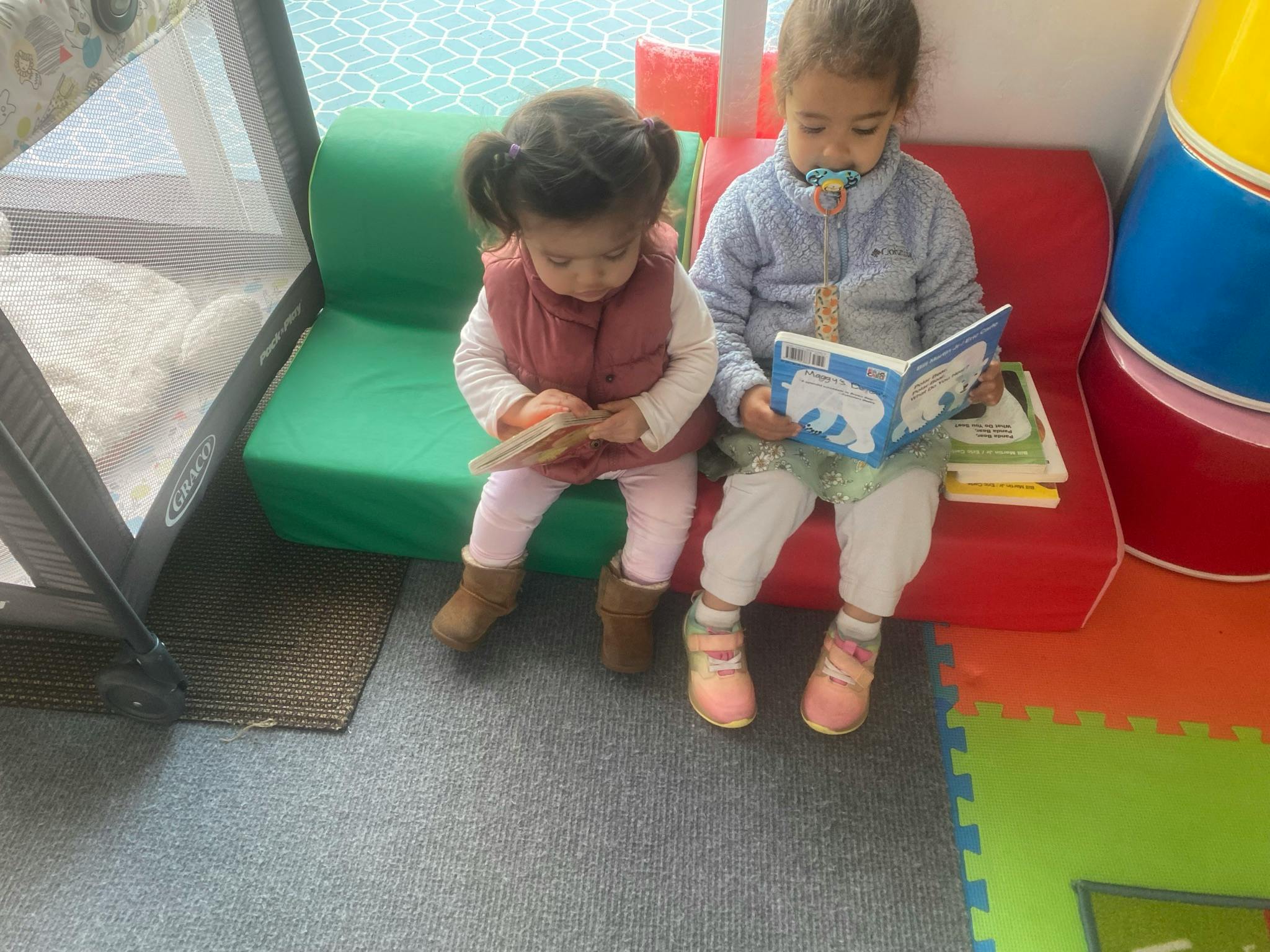 Two children sitting on small chairs reading books