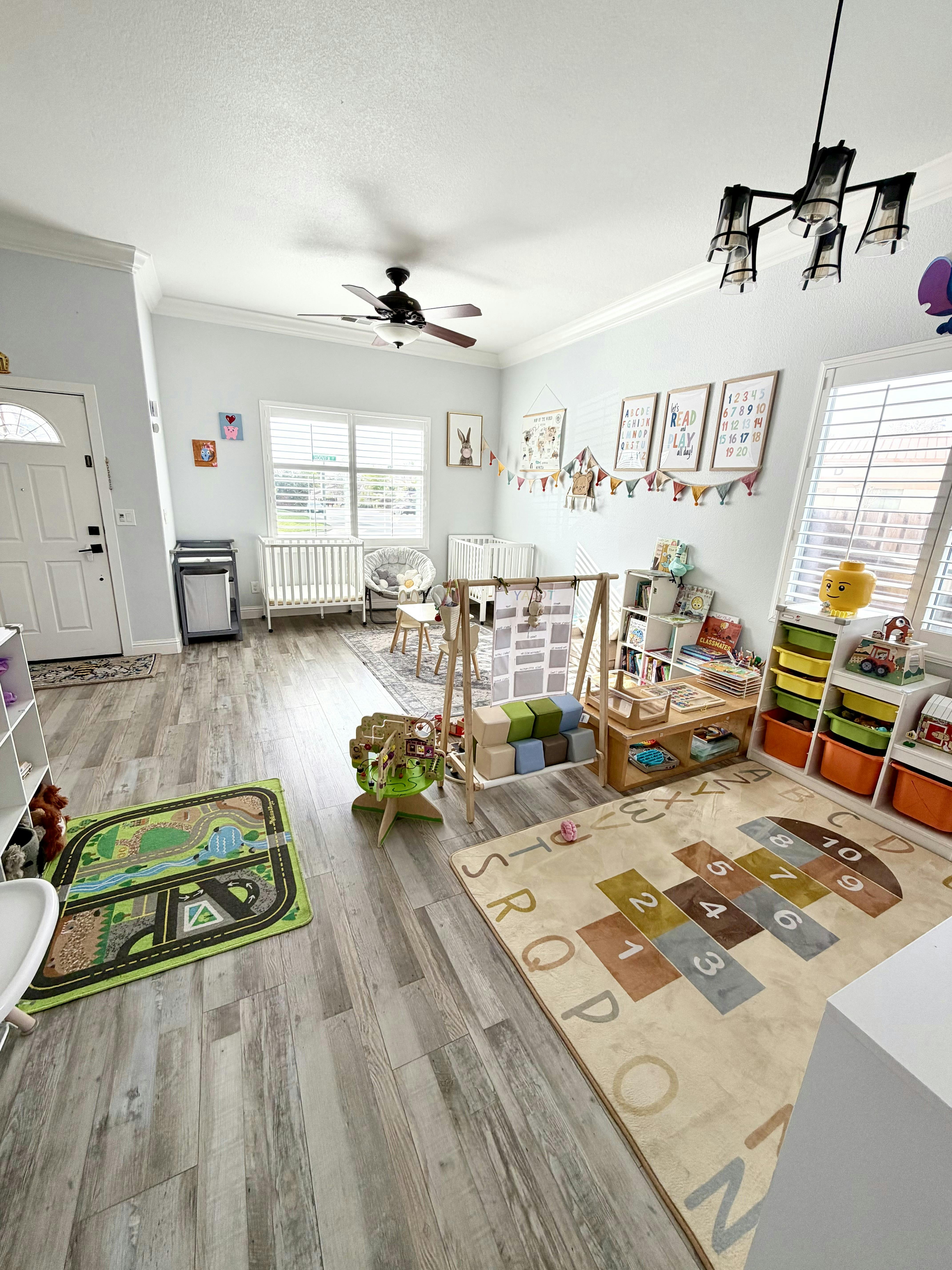 A playroom with two cribs, play mats, bookshelves, and various children's toys