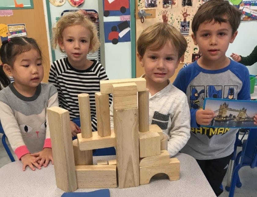 Four children standing around a wooden block structure