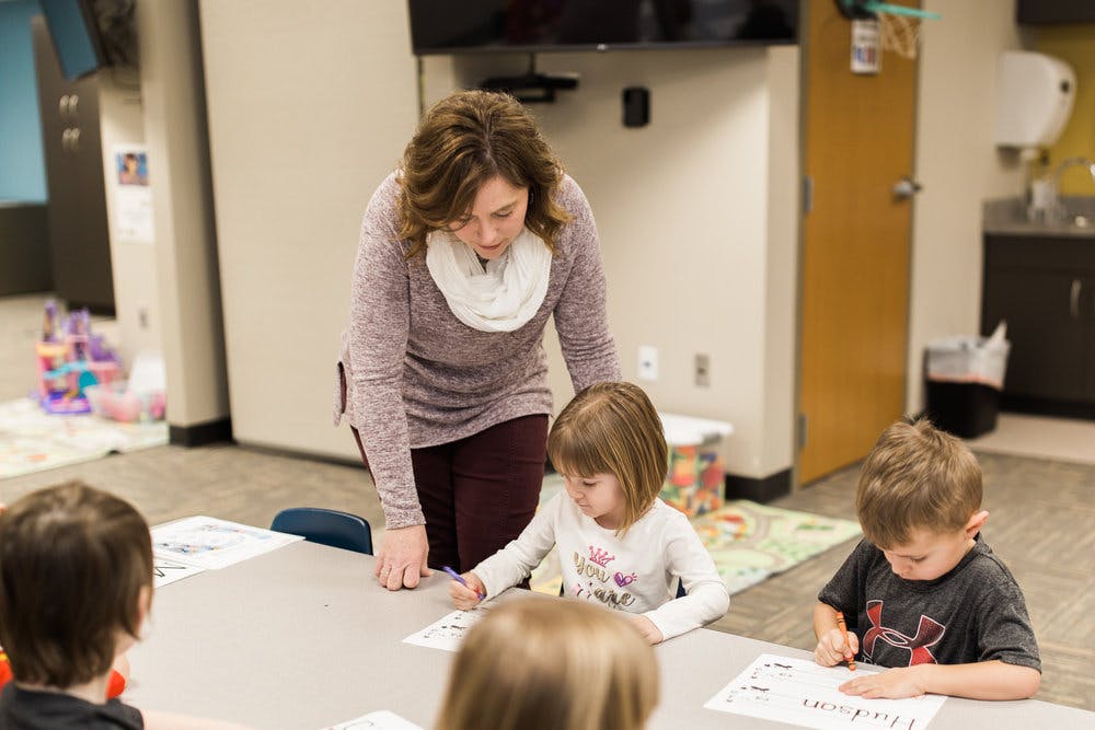 Adult person helping a child with an activity at a table with other children