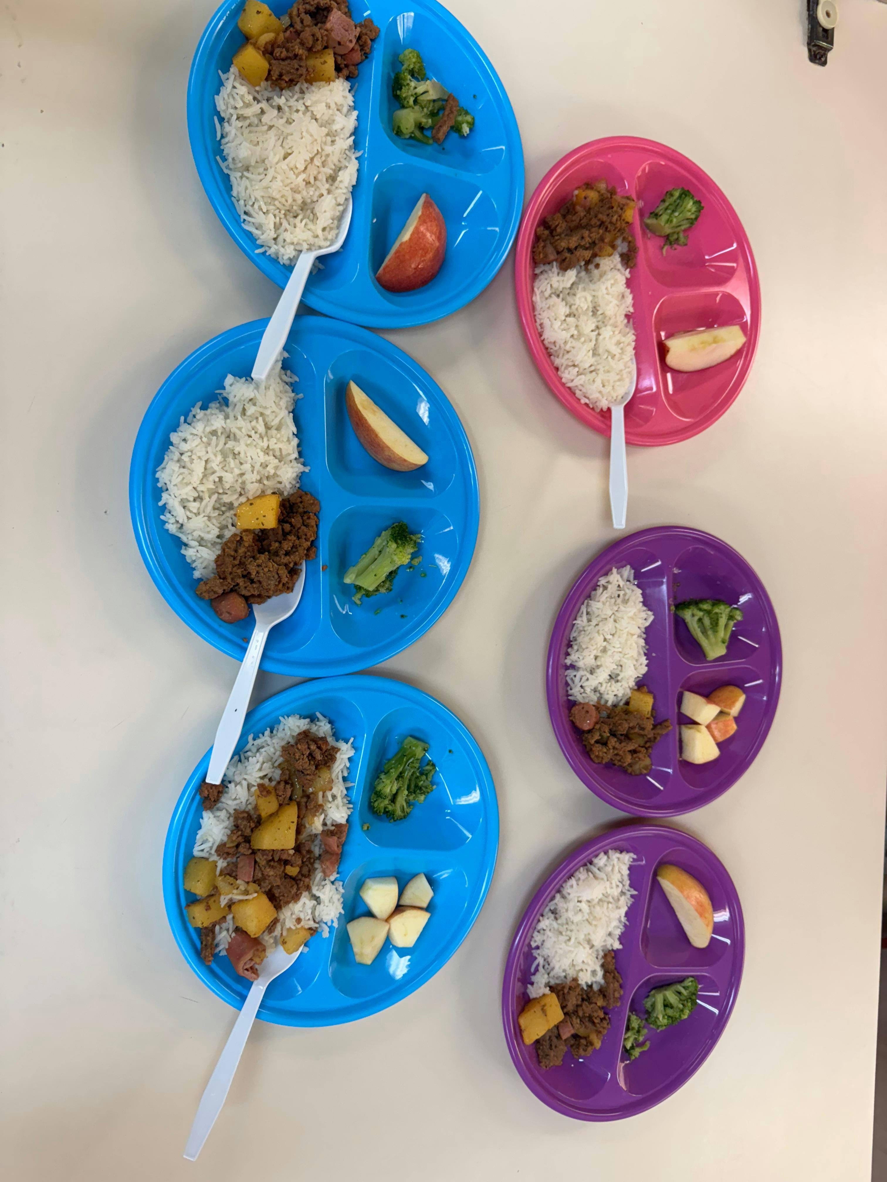 Multiple divided plates with rice, meat, vegetables, and fruit