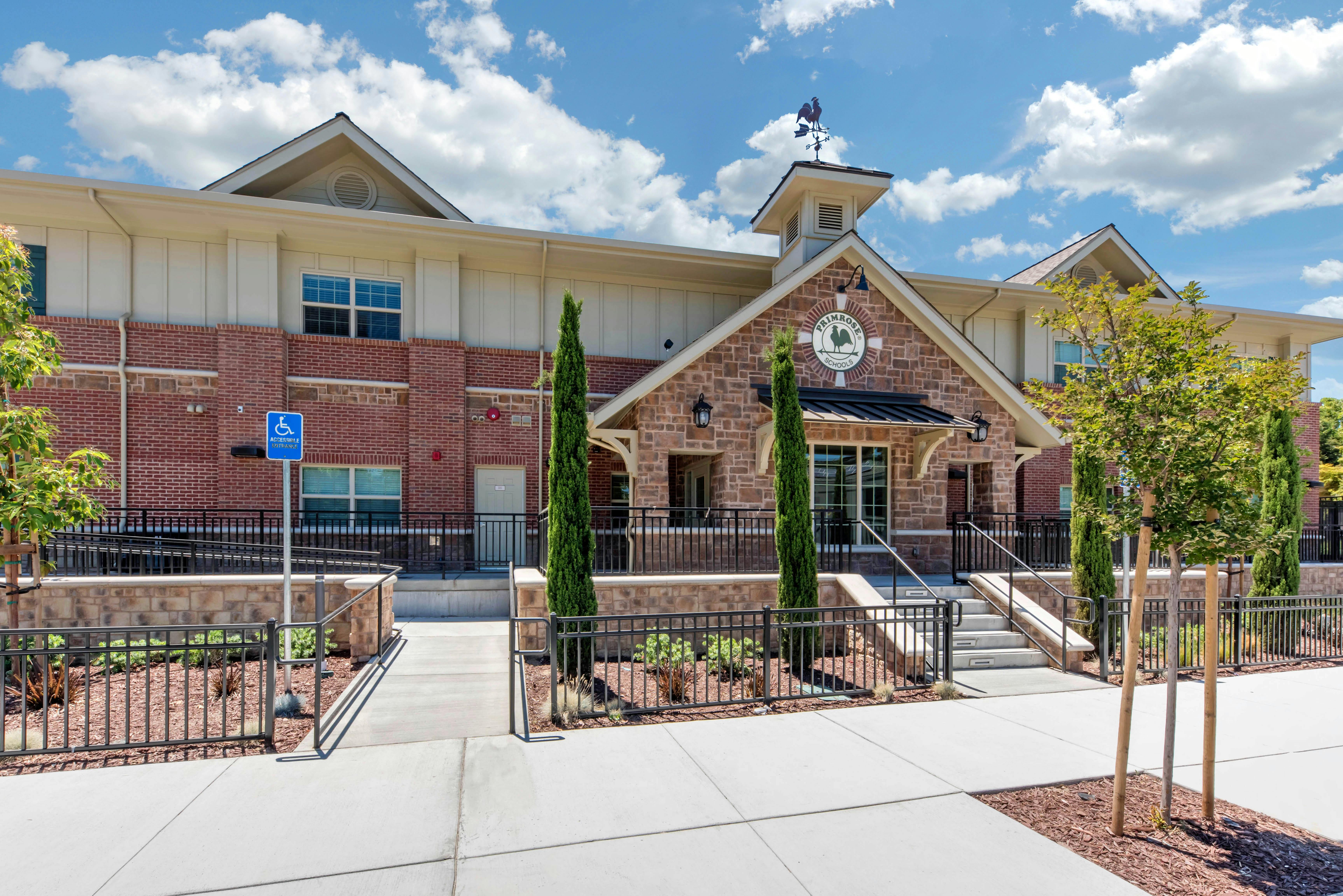 A Primrose School building with a stone facade, red brick walls, and a weathervane