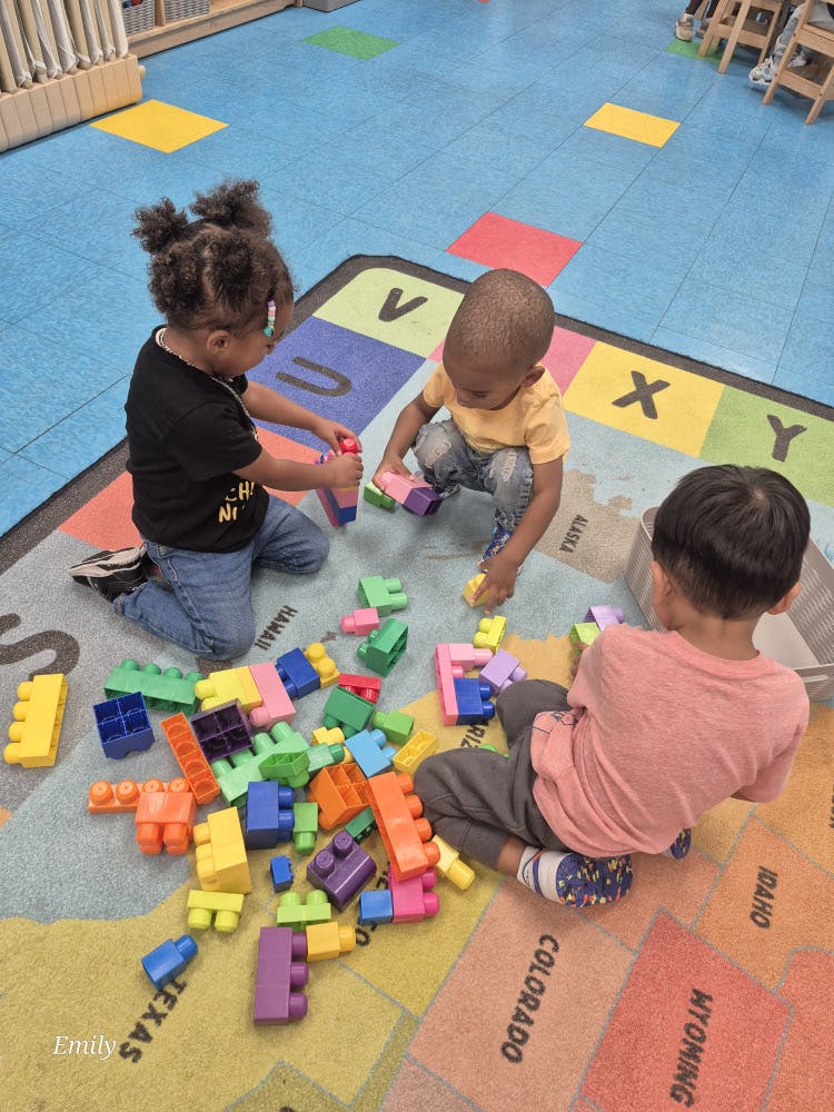 Three children playing with colorful building blocks on a map rug