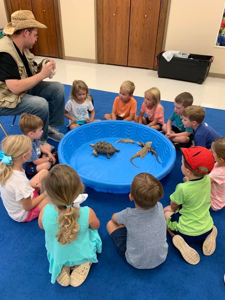 Person in a hat showing reptiles in a blue pool to a group of children