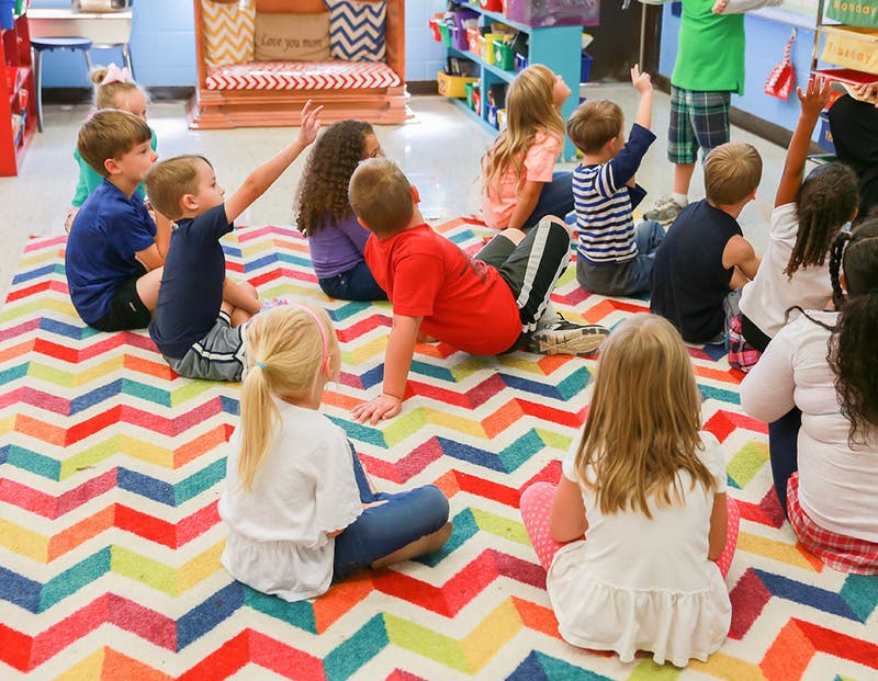 Children sitting on a colorful rug in a classroom