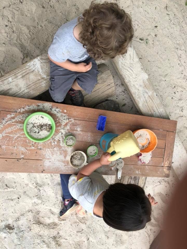 Two children playing with sand and toys on a wooden surface