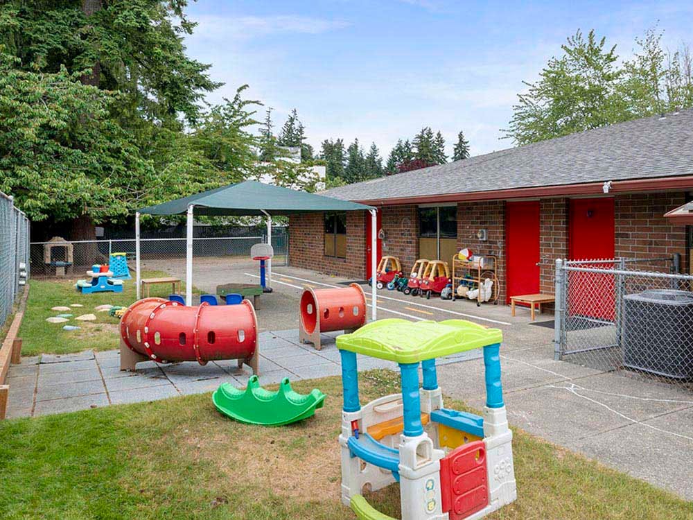 Outdoor play area with small play structures, tunnels, and a shaded sandbox