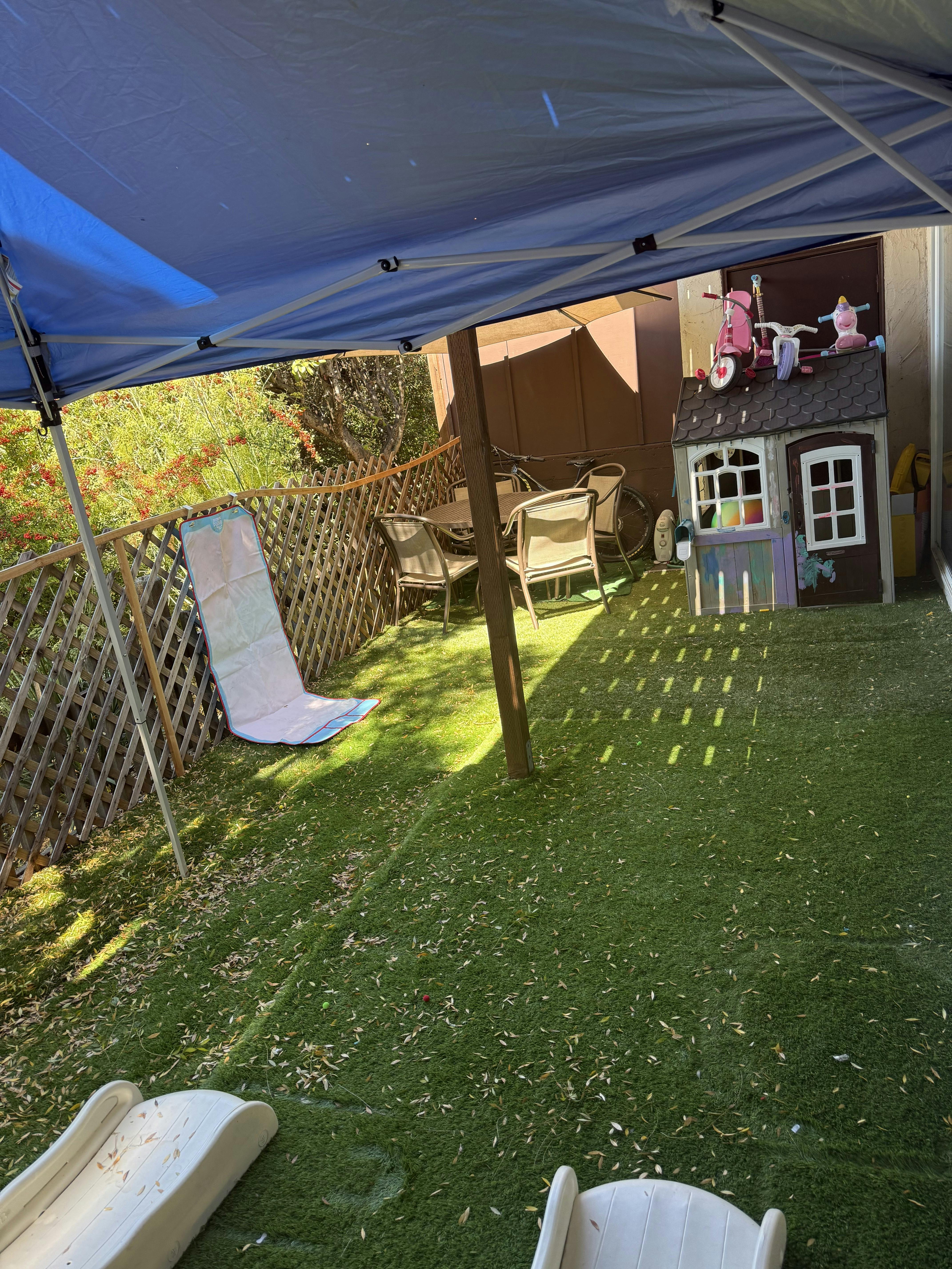 A backyard play area under a canopy with a plastic playhouse and slides