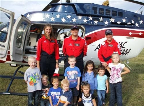 Three adults and multiple children posing in front of a helicopter