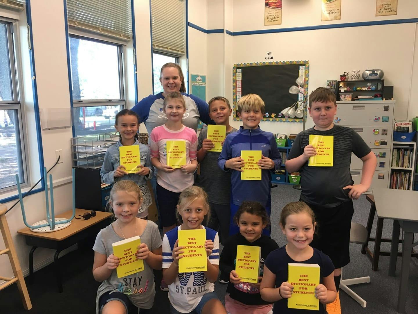 Adult and multiple children holding up yellow papers in a classroom