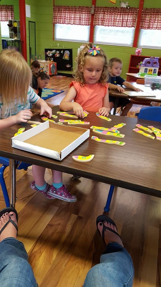 Children playing with puzzle pieces at a table in a classroom