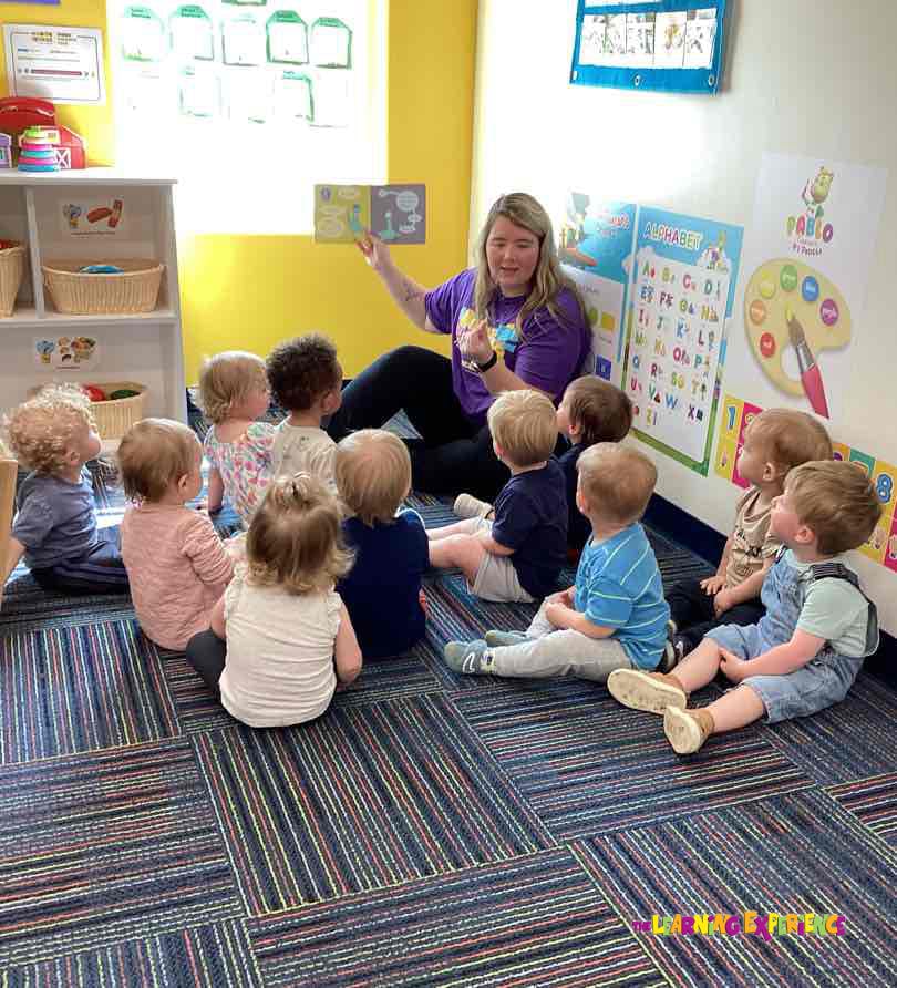 Adult reading a book to a group of children sitting on the floor in a classroom