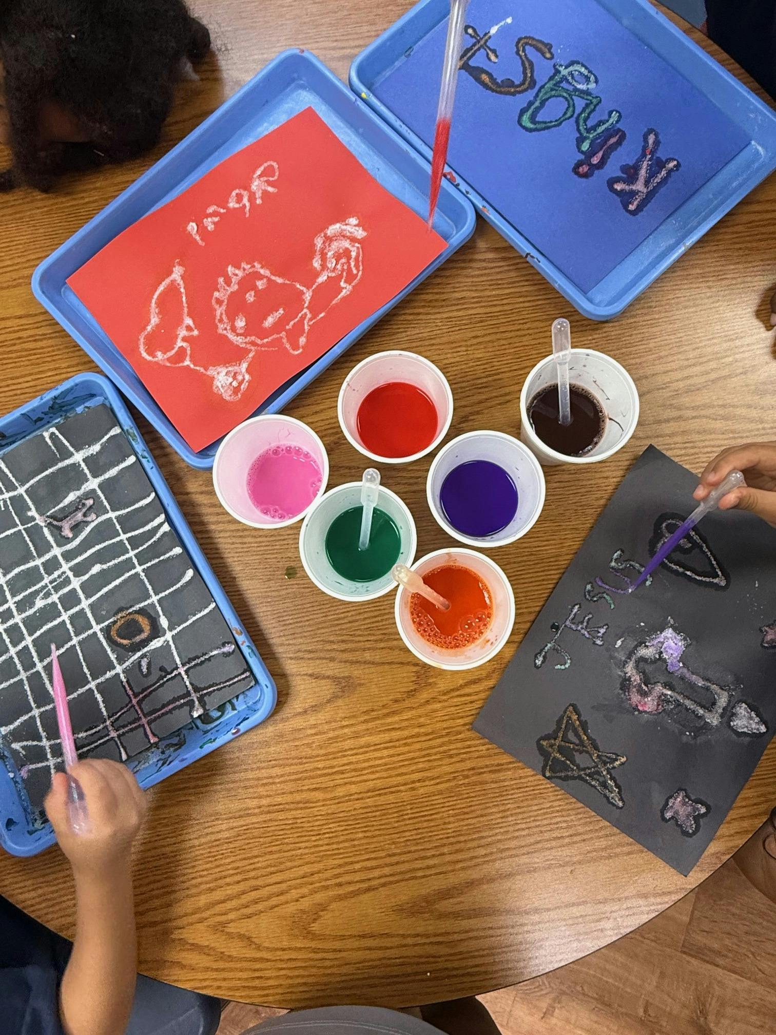 People creating art with pipettes and colorful liquids on paper