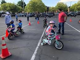 Children on bicycles with adults in a paved area with traffic cones