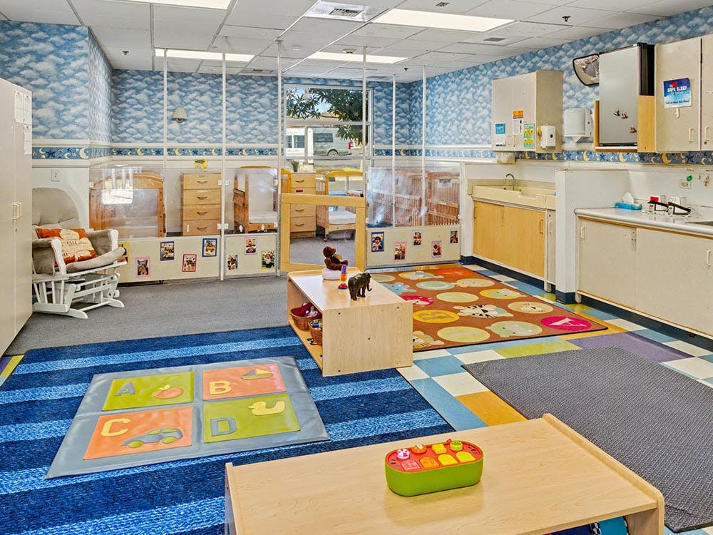 Classroom with multiple cribs, a rocking chair, and play mats on the floor