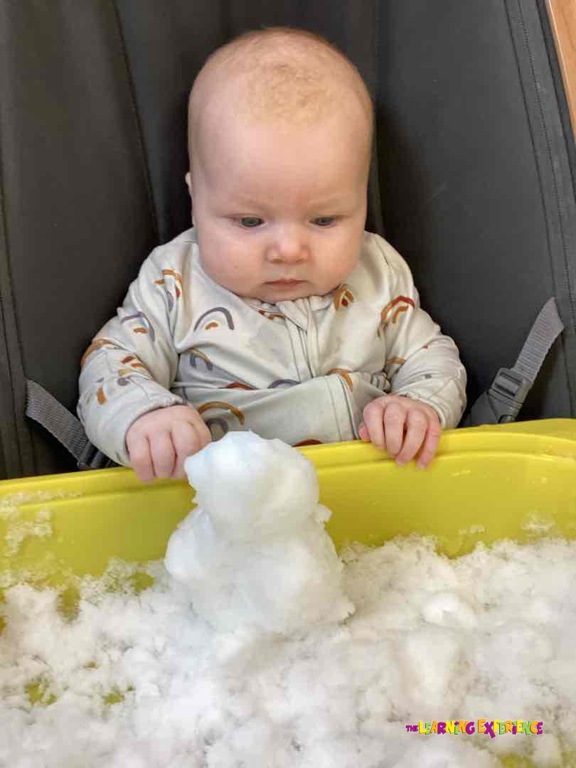 Child in a high chair looking at snow in a yellow bin