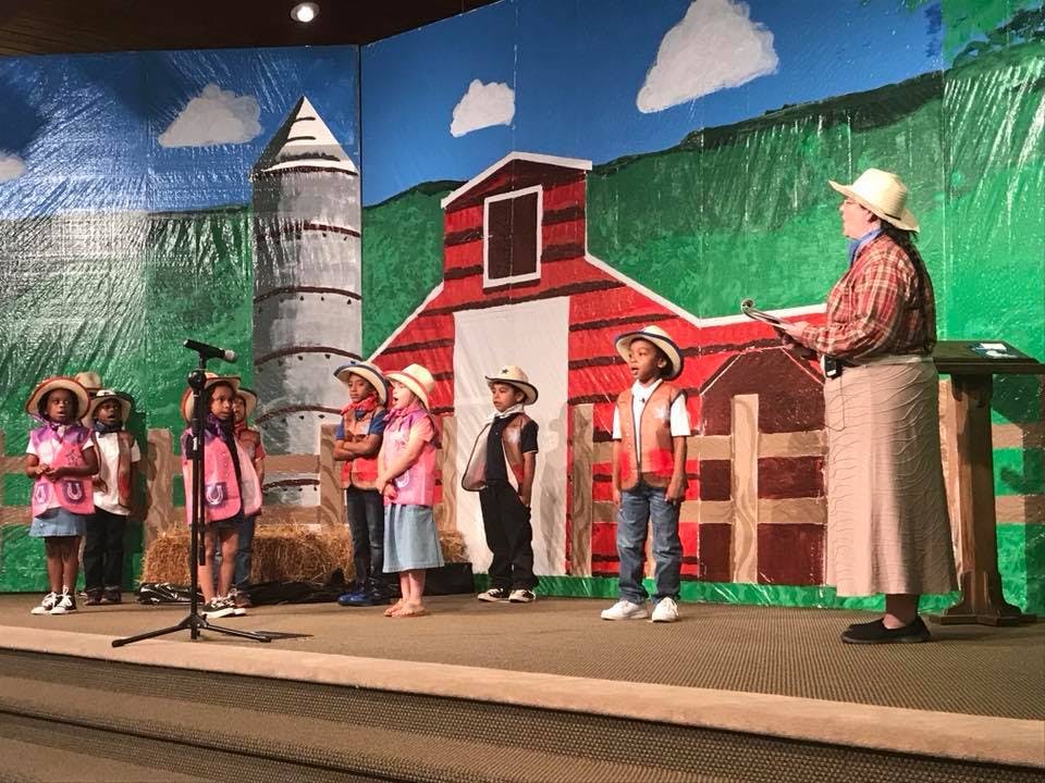 Children and an adult on a stage with a farm-themed backdrop