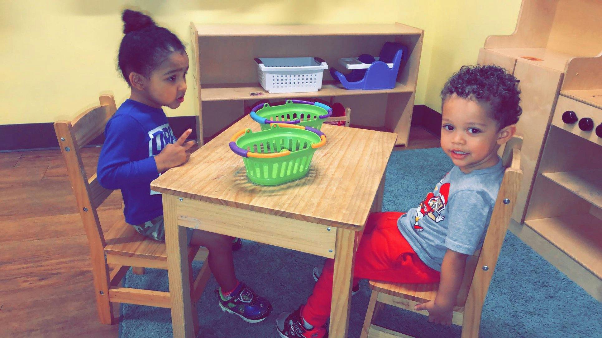 Two children sitting at a small table with green baskets