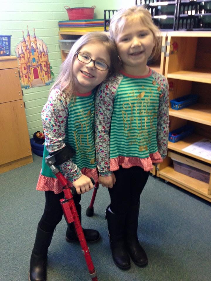Two children standing together, one with a red crutch