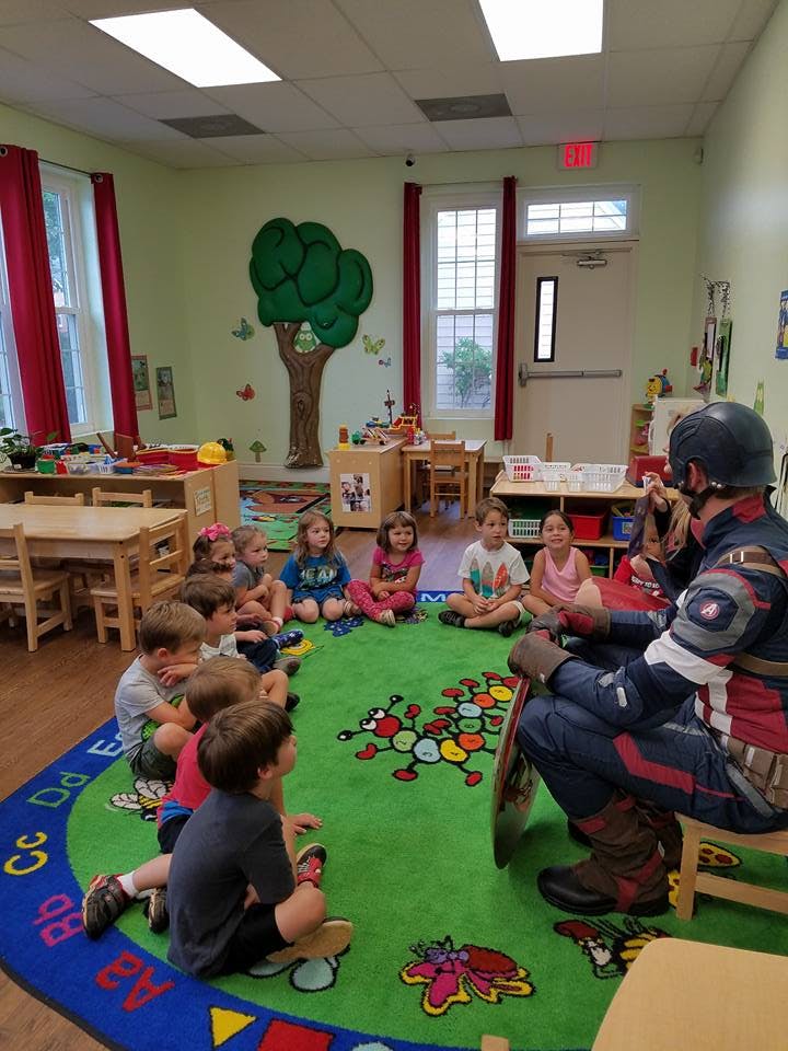 Person in superhero costume sitting with children in a classroom