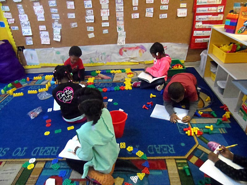 Children sitting on a rug with building blocks and drawing