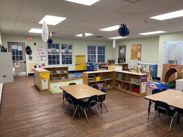 An empty classroom with small tables and chairs, shelves of toys, and decorations