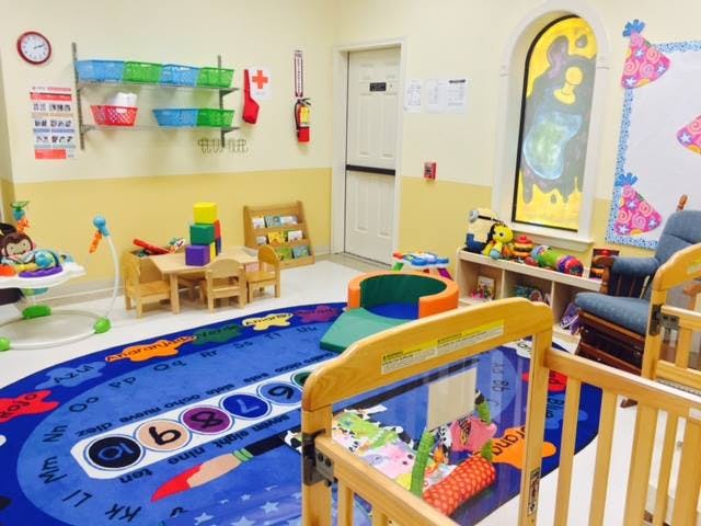 A colorful playroom with a blue rug, small table and chairs, and cribs