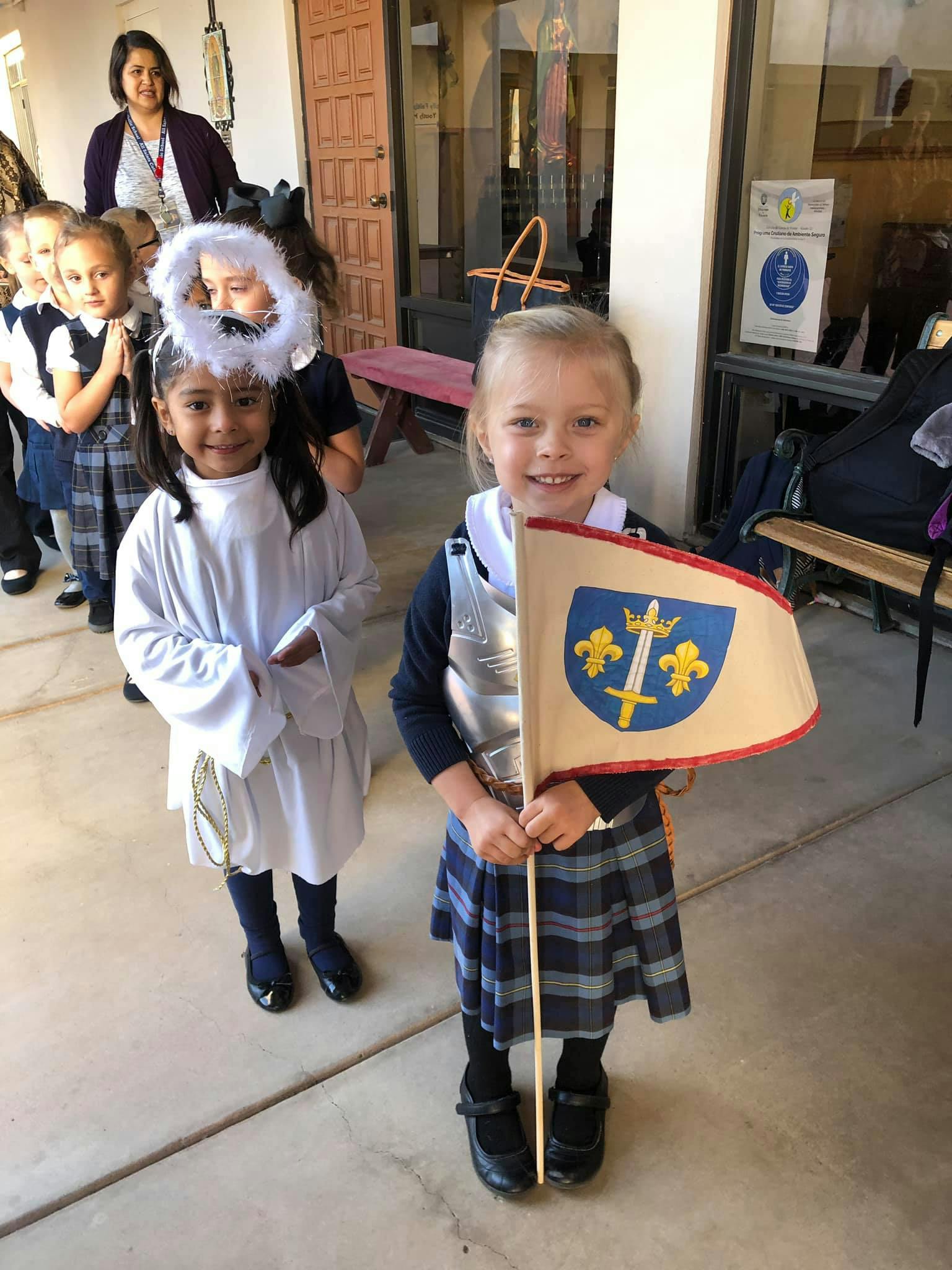 Child in knight costume holding a flag, child in angel costume behind