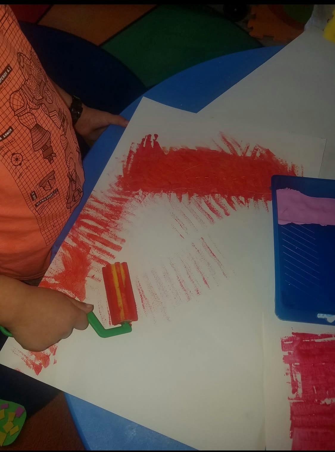 Child painting red paint on paper with a foam roller