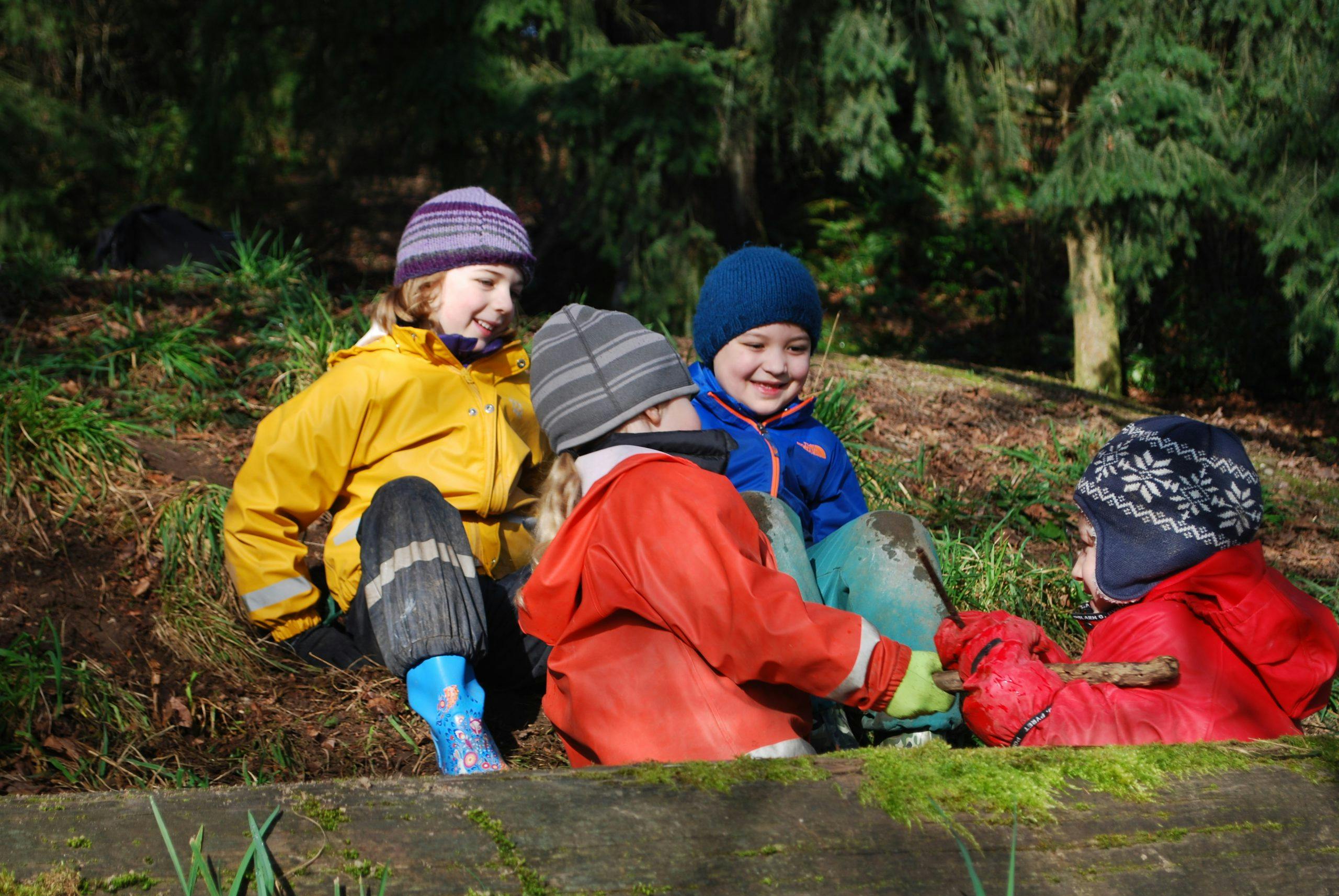 Four children in winter clothing playing on a grassy, muddy hill