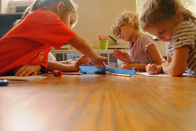 Three children drawing and playing at a table