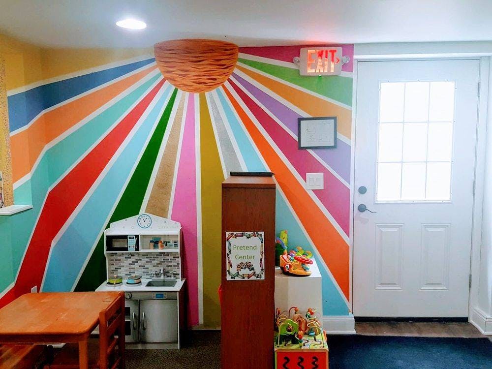 Playroom with colorful striped wall, small table, and toy kitchen